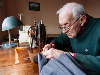 Senior man sewing textile at home