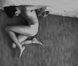 Full length of young man in underwear lying upside down in bed at home