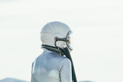 Back view man in spacesuit and helmet looking away while standing on path on sunny day in nature