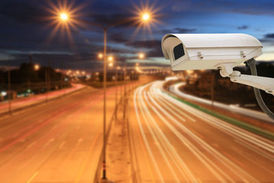 Security camera over light trails on road against sky at dusk