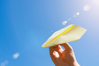 Playing with paper airplane against blue sky and warm summer sun glare