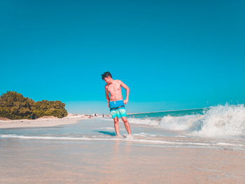 Full length of shirtless man in sea against clear sky