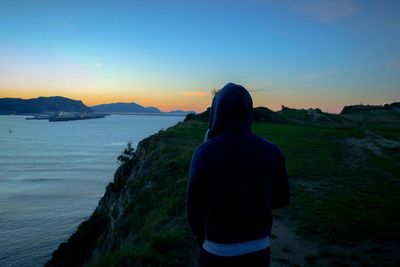 Rear view of man standing against sea at sunset