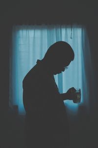 Side view of silhouette woman holding camera at home