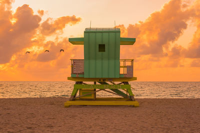 Lifeguard hut on beach against sky during sunset