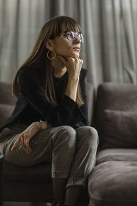 Young woman looking away while sitting on sofa