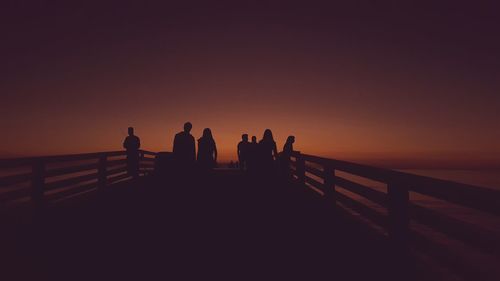 Silhouette people standing by sea against clear sky during sunset