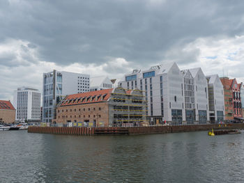 Buildings by river against sky in city