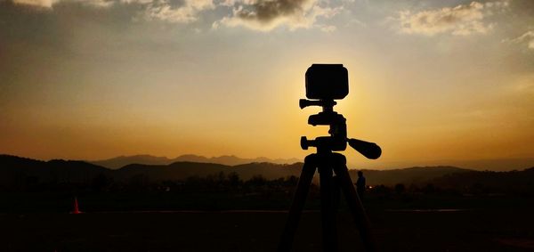 Silhouette camera on field against sky during sunset