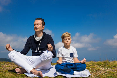 Full length of father and son doing yoga on mountain against sky