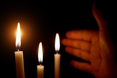 Close-up of hand gesturing by candles against black background