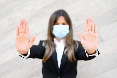 Portrait of businesswoman wearing mask gesturing while standing against wall