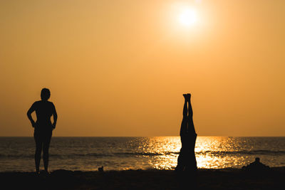 Silhouette people standing on beach against orange sky