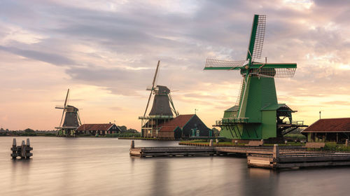 Traditional windmill by lake against sky during sunset