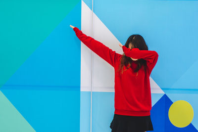 Woman gesturing while standing against blue wall