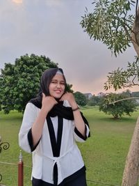 Portrait of smiling young woman standing against trees