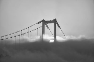 Low angle view of suspension bridge against sky and fog