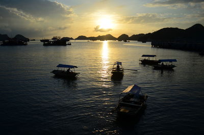 Silhouette boats in river against sky during sunset