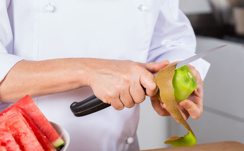 Midsection of chef peeling kiwi in commercial kitchen