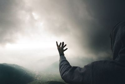 Rear view of man gesturing while standing against cloudy sky