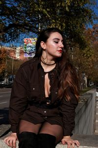 Beautiful young woman sitting against trees in city