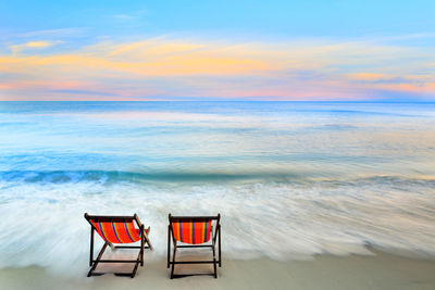 Deck chairs on beach against sky during sunset