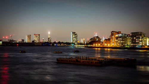 Illuminated buildings by river against sky in city at night
