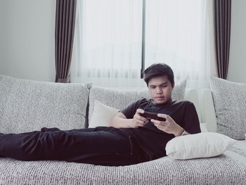 Young man using smart phone while relaxing on sofa at home