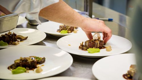 Cropped hand of chef styling food on plate in commercial kitchen