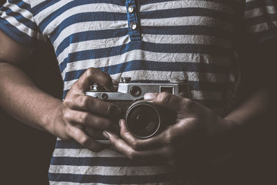 Midsection of man holding camera against black background