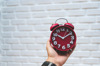 Close-up of hand holding red alarm clock against wall