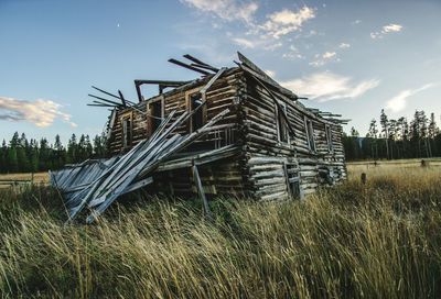 Weathered log cabin on field against sky