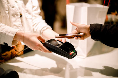 Cropped hand of female customer paying through smart phone at store