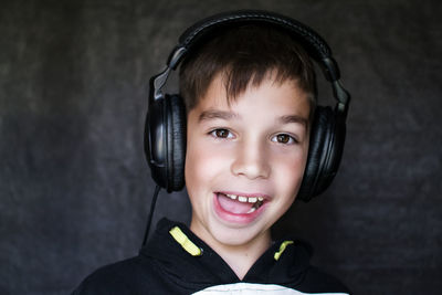 Close-up portrait of boy making face while listening music in headphones against wall