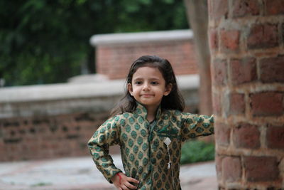 Portrait of smiling girl standing against brick wall