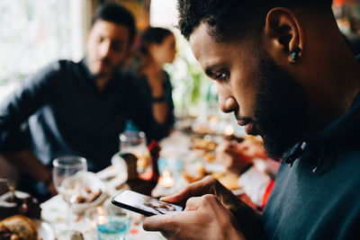 Young man photographing lunch while sitting with friends at restaurant during party