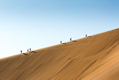 People walking at desert against clear sky