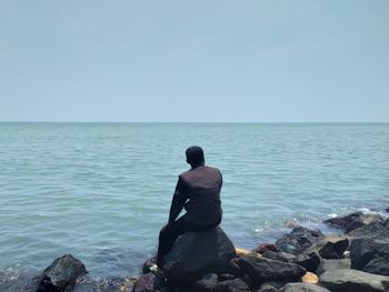 Rear view of man looking at sea against clear sky