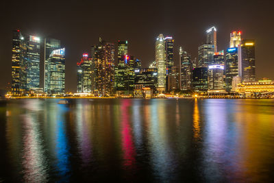 Illuminated buildings by river against sky at night