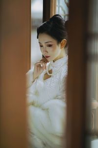 Portrait of woman looking through window at home