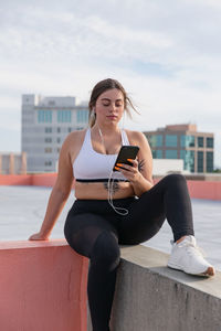 Curvy woman listens to music on mobile phone working out outdoors.