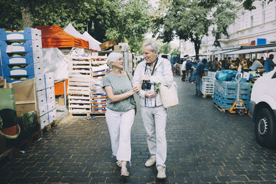 Full length of elderly couple talking while walking arm in arm at street market