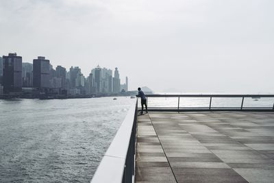 Rear view of man on sea by buildings against sky