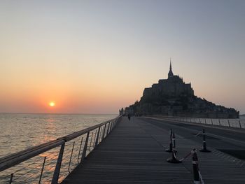 People walking on pier over sea against clear sky during sunset