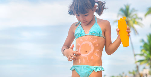 Girl applying sunscreen on stomach at beach