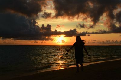 Silhouette woman walking at beach during sunset