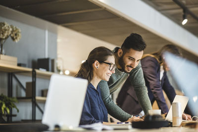 Smiling businesswoman and coworker working over laptop at creative office