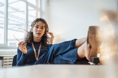 Carefree customer service representative holding eyeglasses talking through headset sitting with feet up at desk