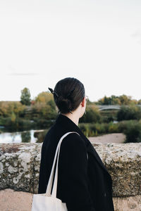 Side view of young woman standing against sky