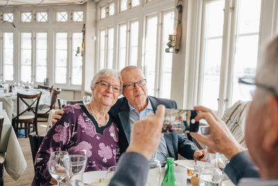 Male friend clicking photograph of senior couple in restaurant